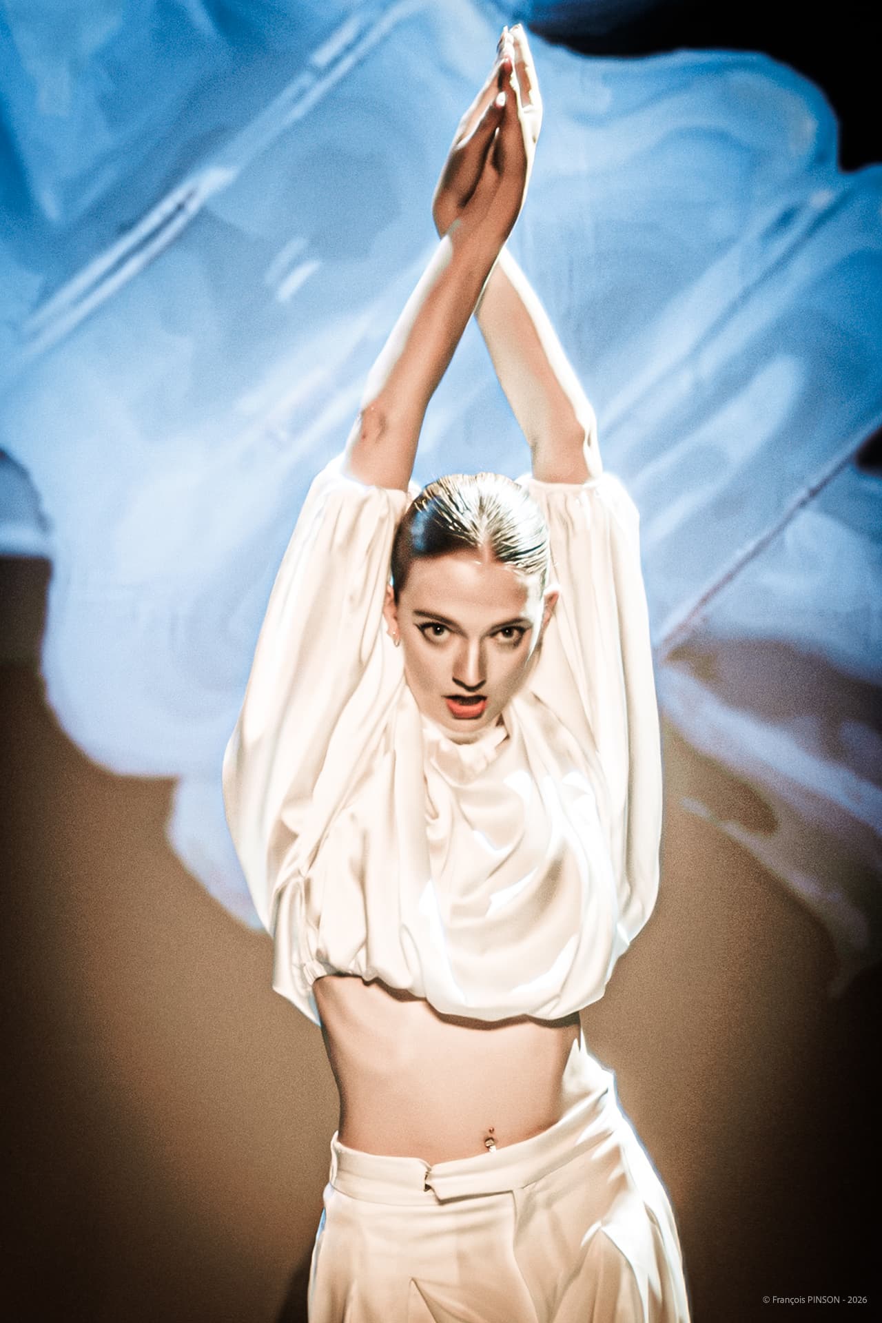 Danseuse Krisaor en costume blanc, bras levés, sur la scène du spectacle 2026 — photographie François Pinson